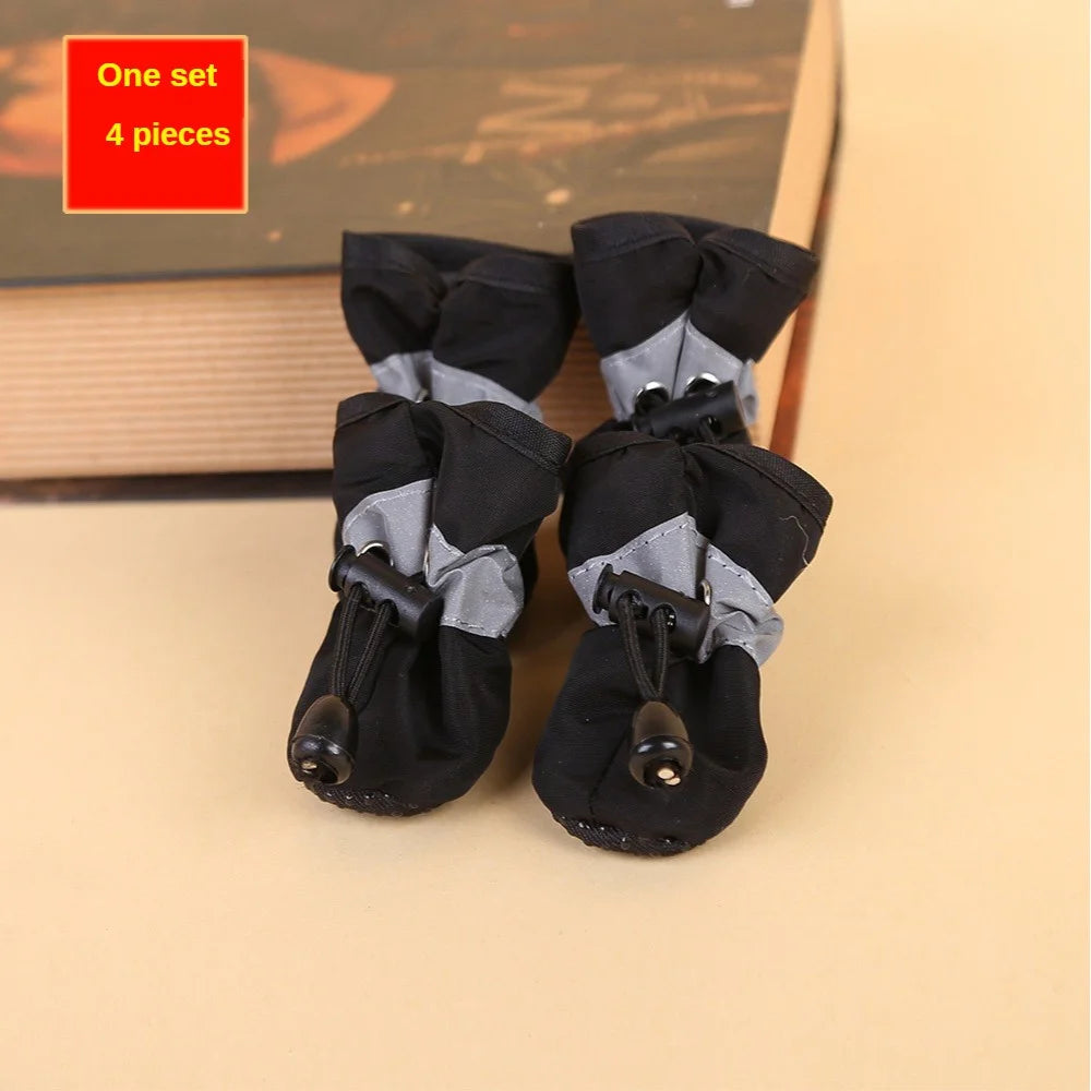 Set of four black pet boots with gray cuffs on a beige surface.