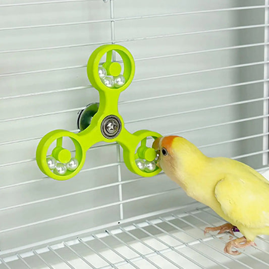 Yellow parakeet interacting with a green fidget spinner toy inside a birdcage.