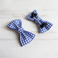 Two blue and white checkered bow ties on a light wooden surface