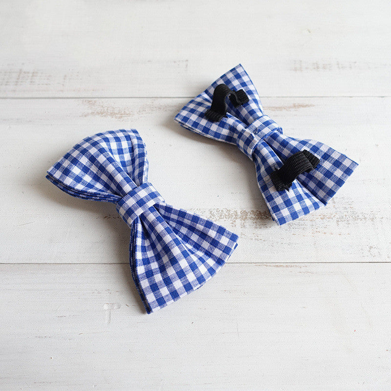 Two blue and white checkered bow ties on a light wooden surface