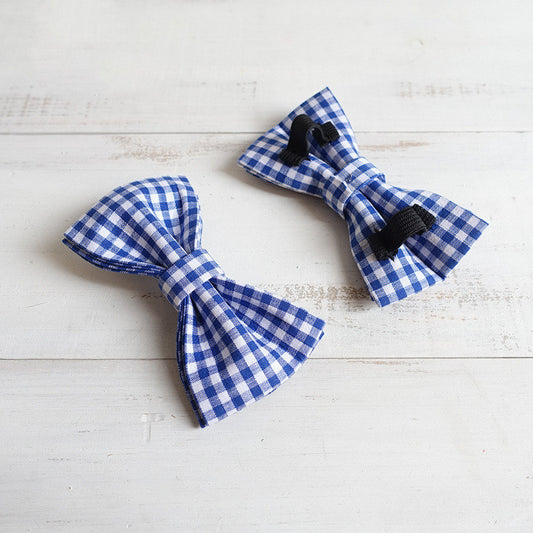 Two blue and white checkered bow ties on a light wooden surface