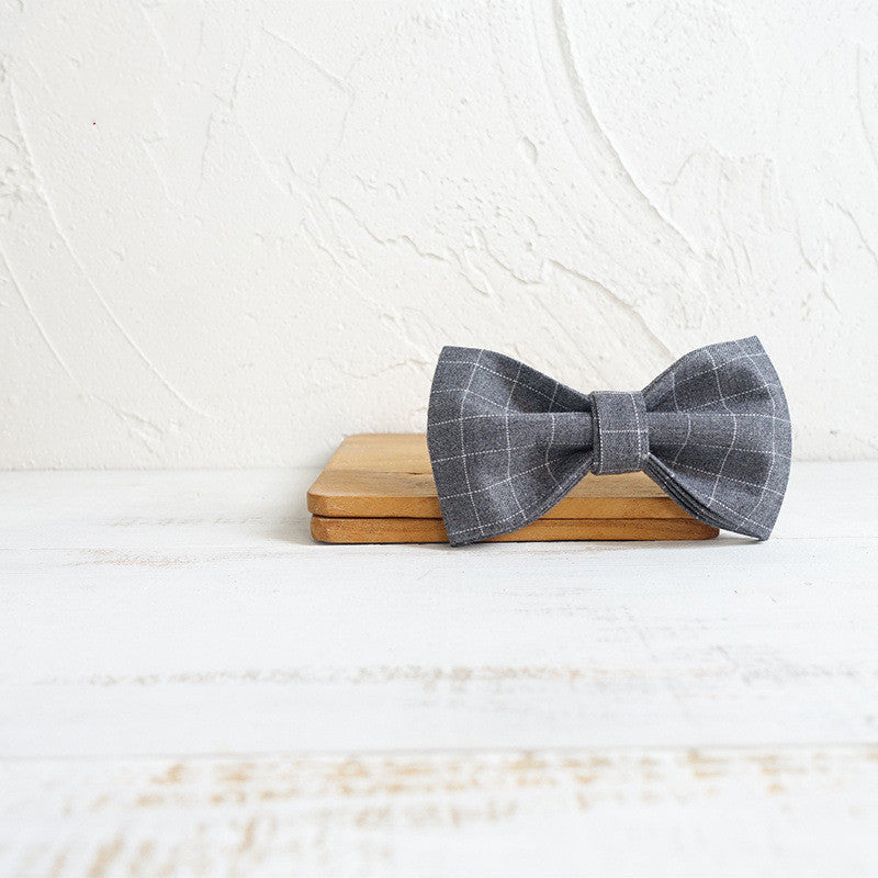 Gray checkered bow tie on a wooden block with a white textured background