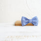 Blue and white checkered bow tie on a wooden block with a white textured background