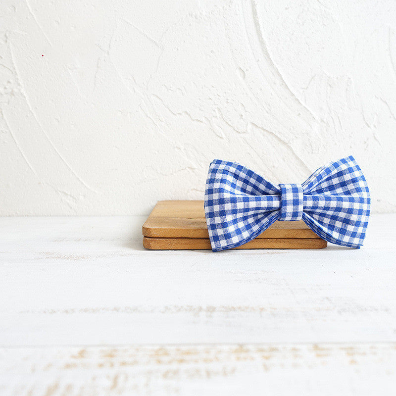 Blue and white checkered bow tie on a wooden block with a white textured background