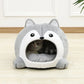 Cat peeking out from a gray pet bed with cartoon face design on a wooden floor.