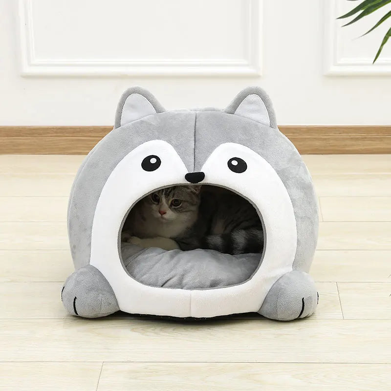 Cat peeking out from a gray pet bed with cartoon face design on a wooden floor.