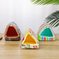 Three colorful pet houses on a wooden surface with a white textured wall and green leaves in the background.
