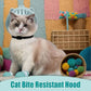 Cat wearing a bite-resistant hood with colorful toys and a textured wall in the background