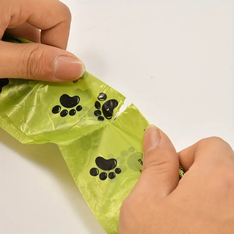 Green plastic bag with black paw prints held by a hand on a white background
