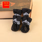Set of four black pet boots with gray cuffs on a beige surface.