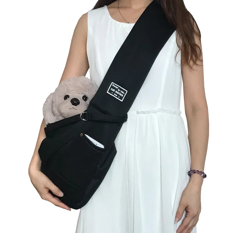 Person wearing a black pet sling with a small gray dog inside, on a white background