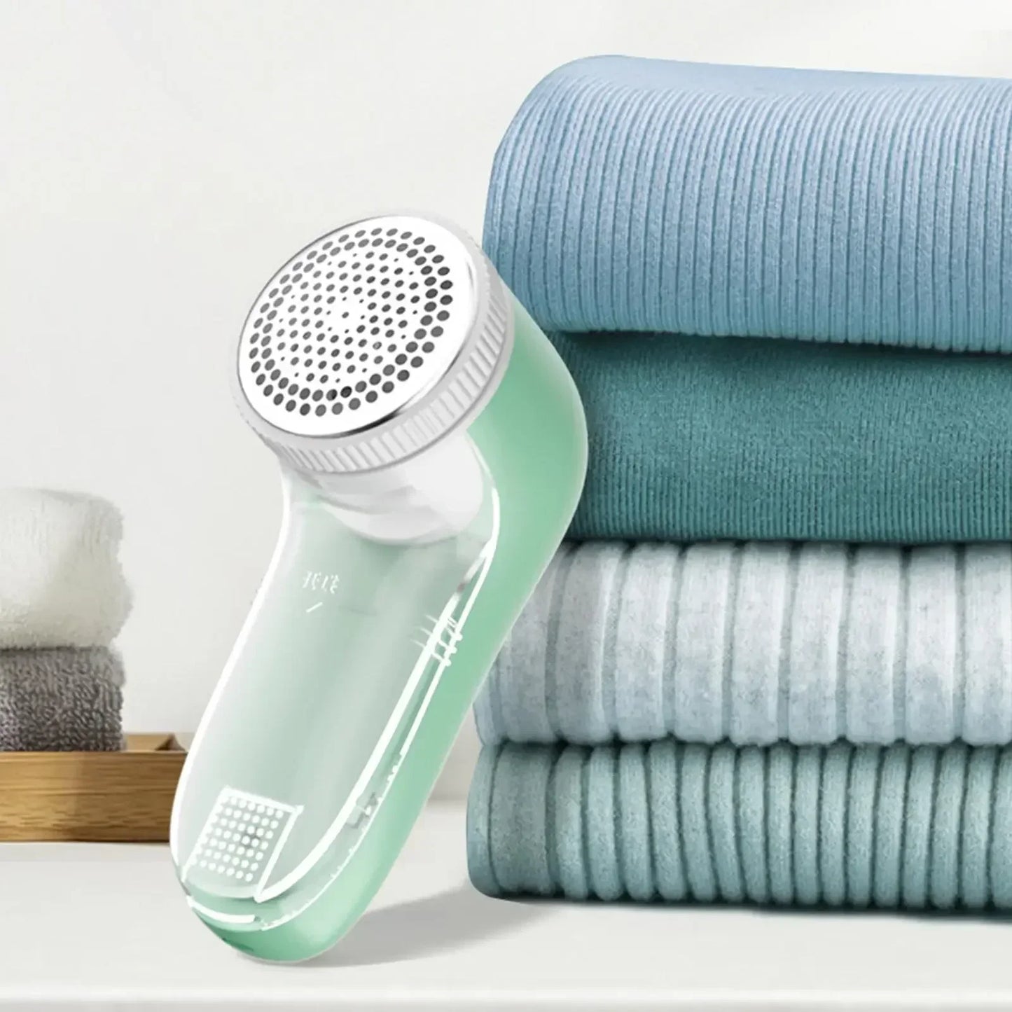Green fabric shaver next to folded clothes on a white background