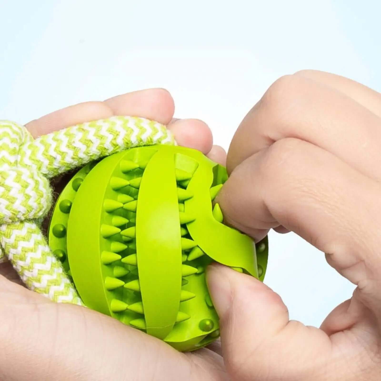 Green dog toy with a rope being held by hands against a light blue background