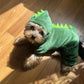 Small dog wearing a green dinosaur costume on a wooden floor