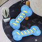 Blue and yellow dog toy shaped like a bone on a dark surface with a plant in the background.