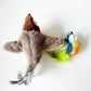 Plush toy resembling a shark with a colorful bird-like figure on a white background