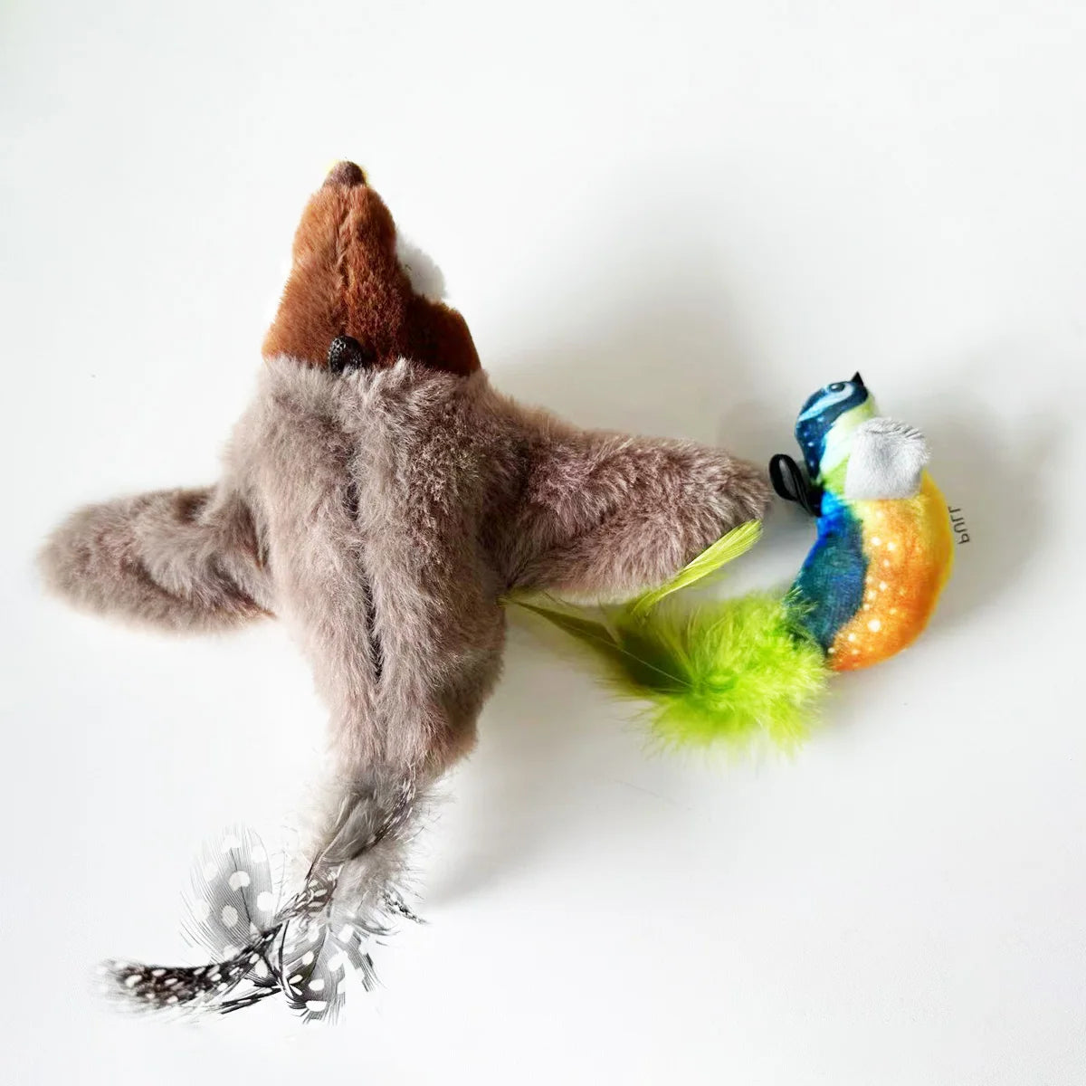 Plush toy resembling a shark with a colorful bird-like figure on a white background