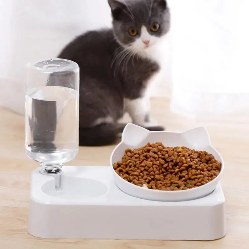 Cat sitting next to a white cat-shaped water dispenser and food bowl on a light wooden floor.