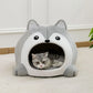 Cat lying inside a gray pet bed shaped like a wolf's head on a light-colored floor.