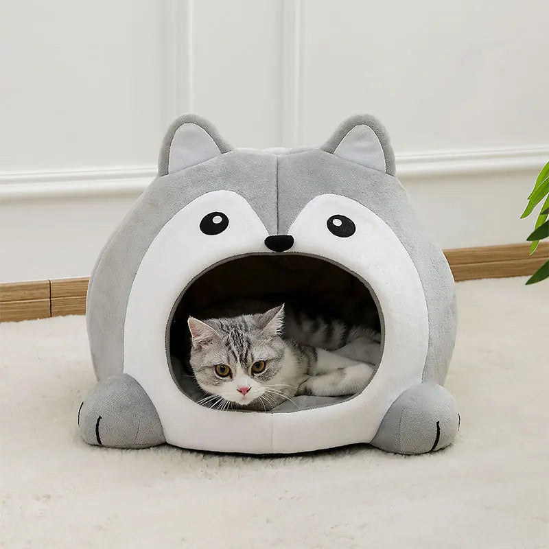 Cat lying inside a gray pet bed shaped like a wolf's head on a light-colored floor.