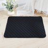 Black quilted mat on a light wooden floor with a plant and white lace fabric in the background.