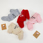 Four children's outfits in gray, red, pink, and beige with text on a white background.