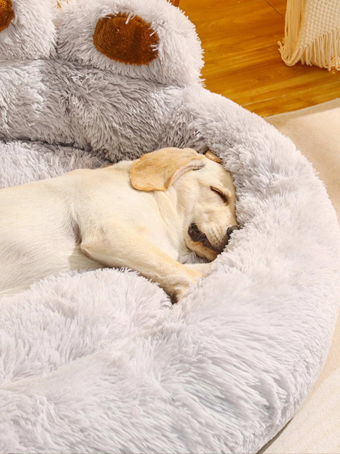 Dog sleeping in a fluffy white pet bed with a soft toy in the background.