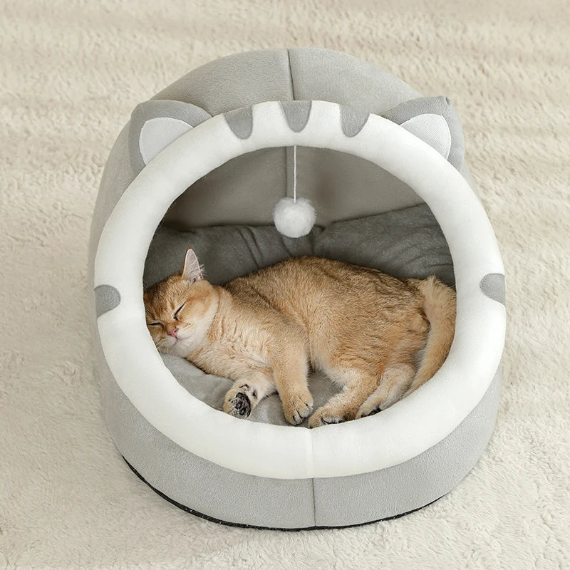 Cat sleeping in a gray pet bed with a white ball toy on a beige carpet.