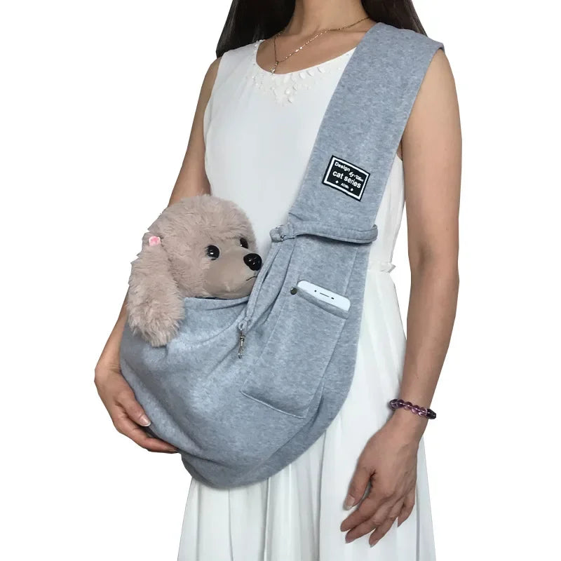 Person holding a gray pet sling with a small dog inside on a white background
