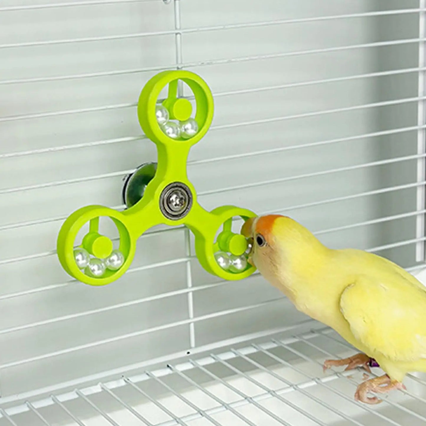 Yellow parakeet interacting with a green fidget spinner toy inside a birdcage.