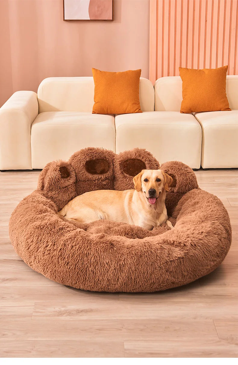 Dog lying on a brown fluffy pet bed in a living room with a beige sofa and orange cushions.