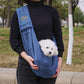 Person holding a small white dog in a blue sling outdoors.