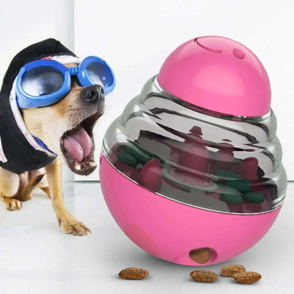 Dog wearing goggles next to a pink and silver ball with treats inside on a white background