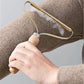 Person using a fabric shaver on a piece of clothing against a neutral background