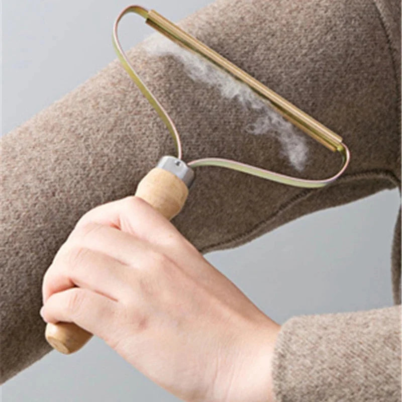 Person using a fabric shaver on a piece of clothing against a neutral background