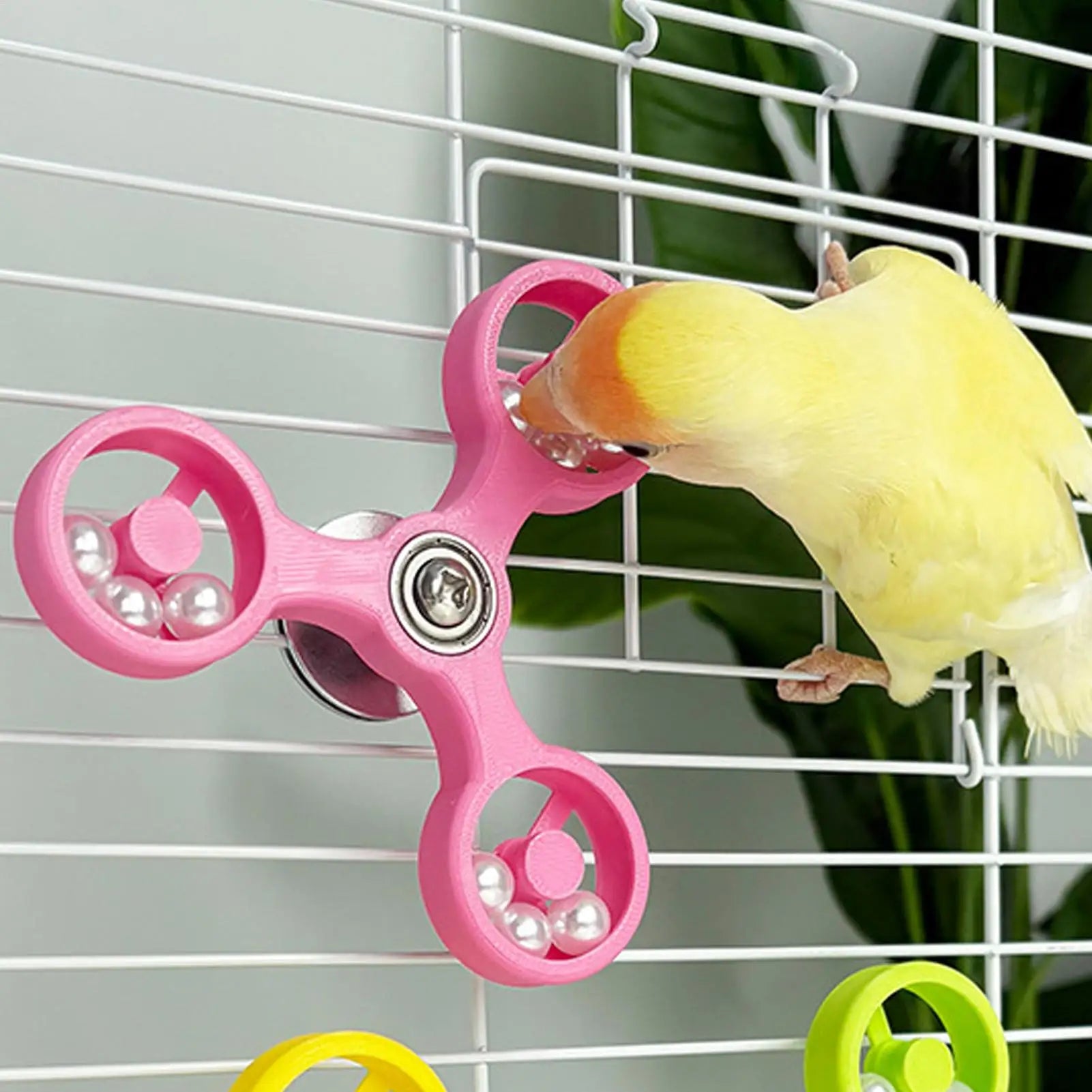 Pink fidget spinner with beads inside a birdcage, with a yellow parakeet interacting with it.