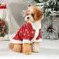 Dog wearing a red Christmas sweater with snowflakes in front of a decorated Christmas tree.