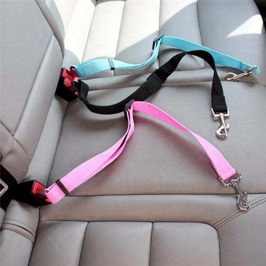 Two dog seat belts, one pink and one black with a blue handle, on a car seat.