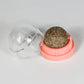 Gold glittery sphere in a pink container with a clear lid on a light gray background