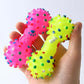 Colorful dog toys shaped like bones held in a hand against a white background