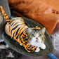 Cat peeking out from a tiger-striped cat bed with a brown cushion in the background