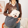 Person holding a small white dog in a gray pet sling indoors.