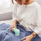 Person using a turquoise garment steamer on a blue sweater.