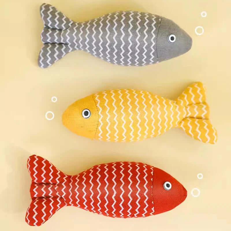 Three fish-shaped toys in gray, yellow, and red on a beige background
