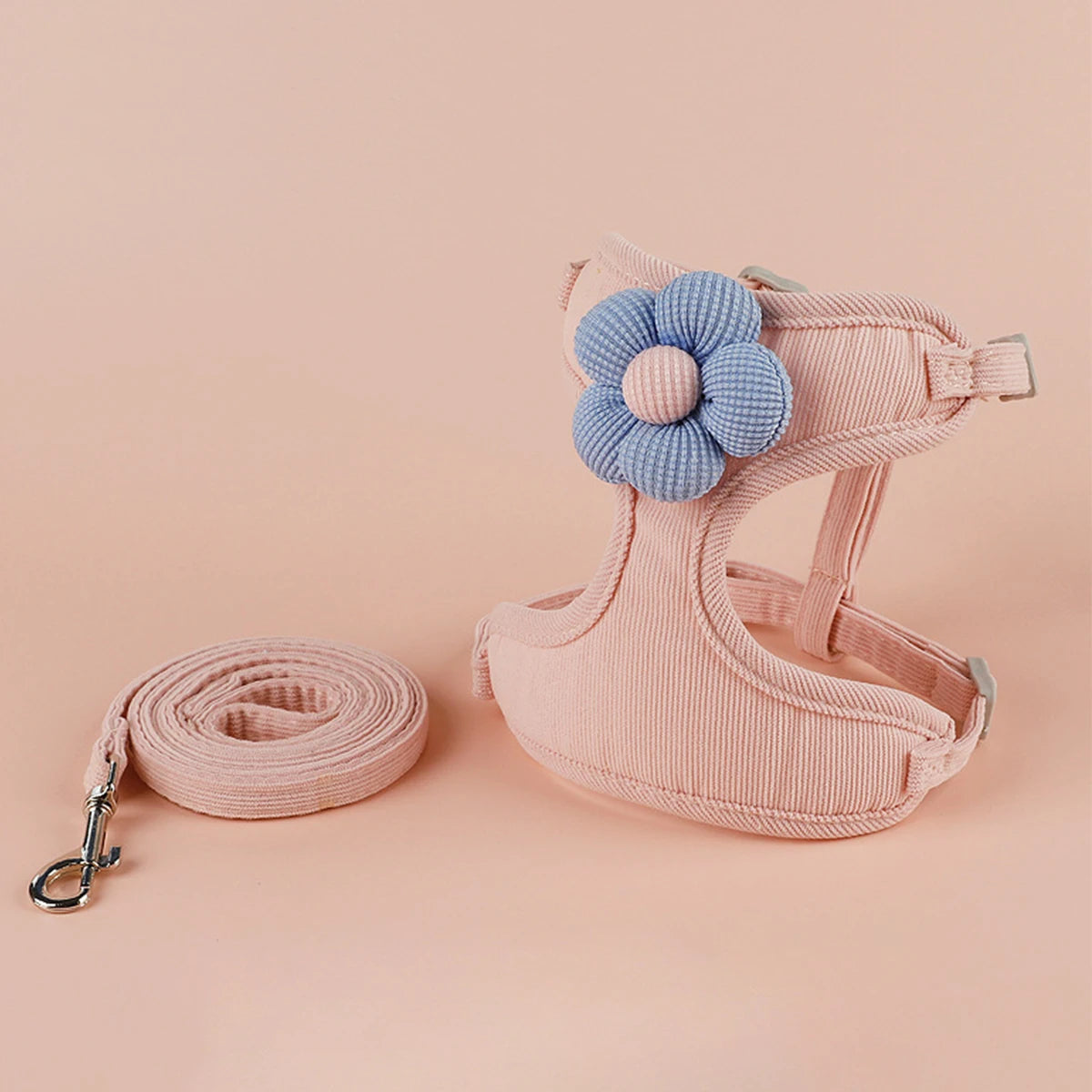 Pink dog harness with a blue flower and matching leash on a pink background