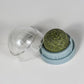 Green glittery ball in a clear plastic container on a white background