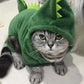 Cat wearing a green dinosaur costume on a light-colored floor.