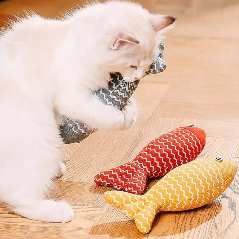 White cat playing with red and yellow striped fish-shaped toys on a wooden floor.