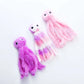 Three plush toy octopuses in pink, purple, and white on a white background