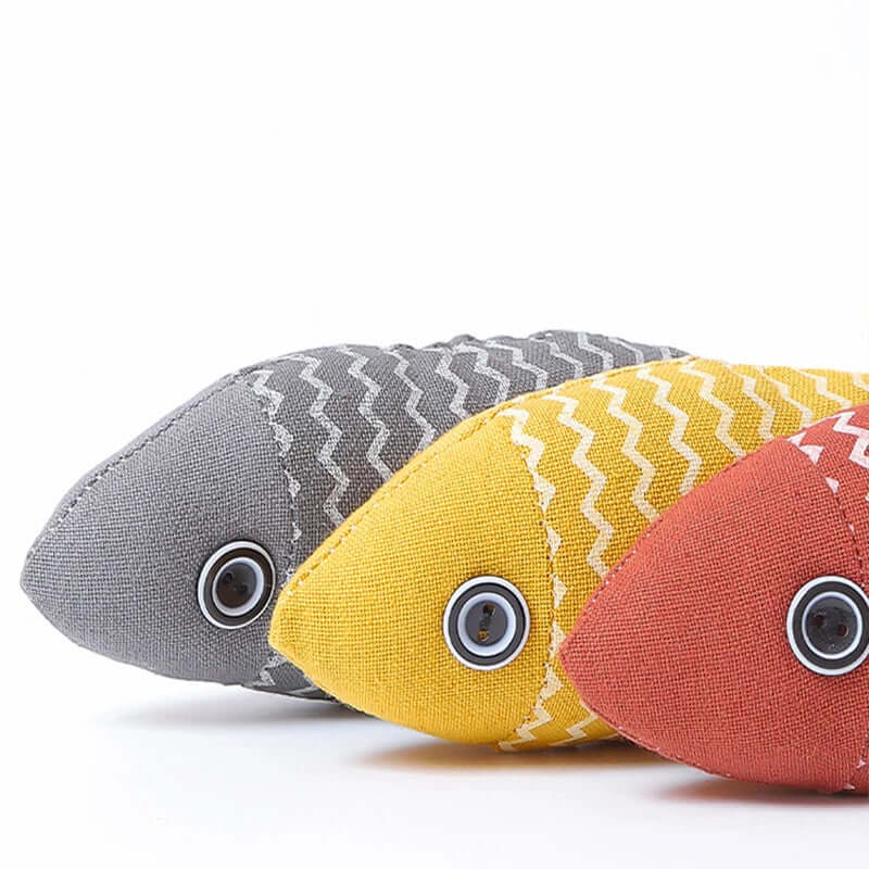 Three fabric fish toys in gray, yellow, and red on a white background